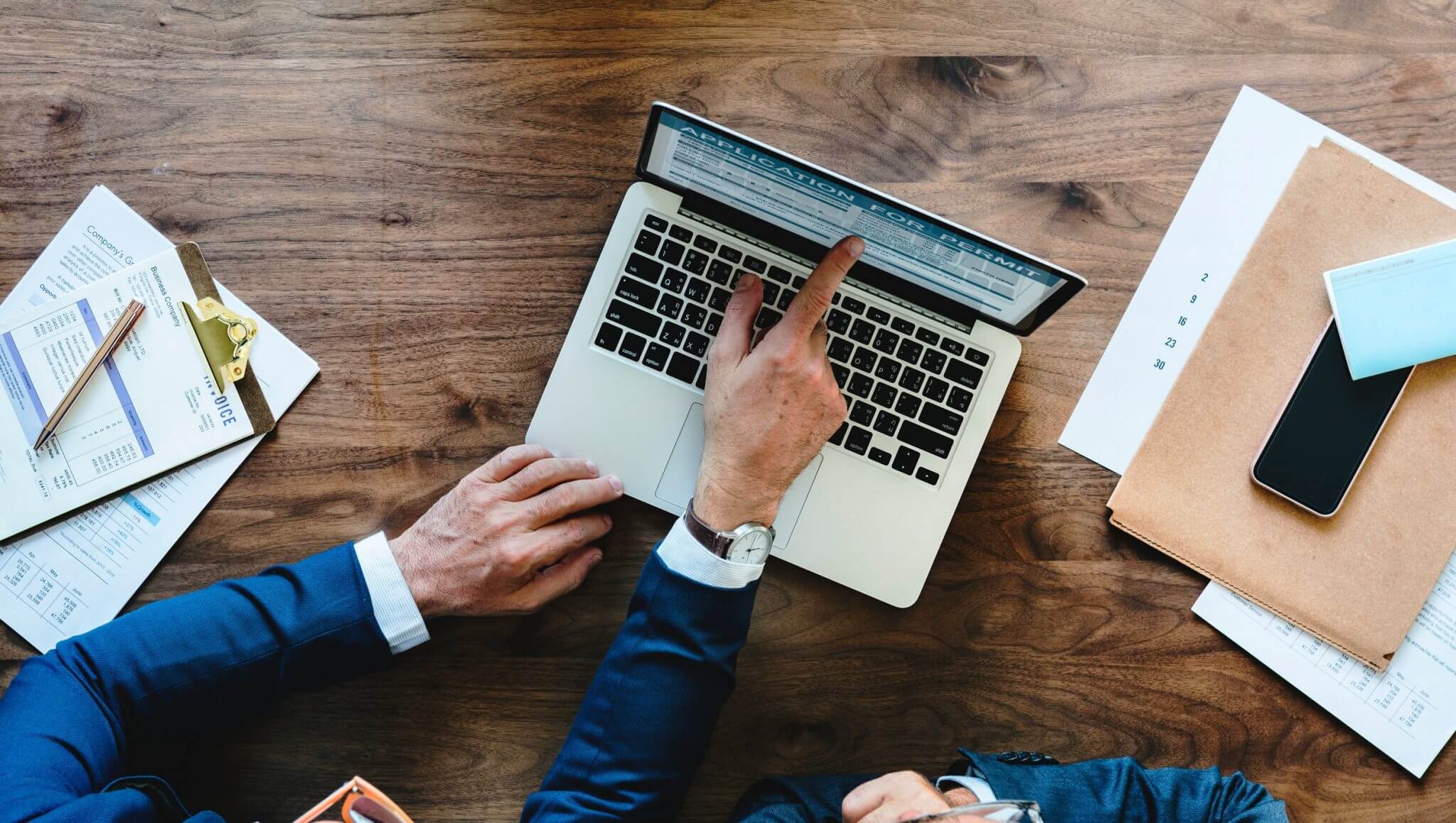 Businessman pointing at something on the screen of his laptop to someone sitting next to him.