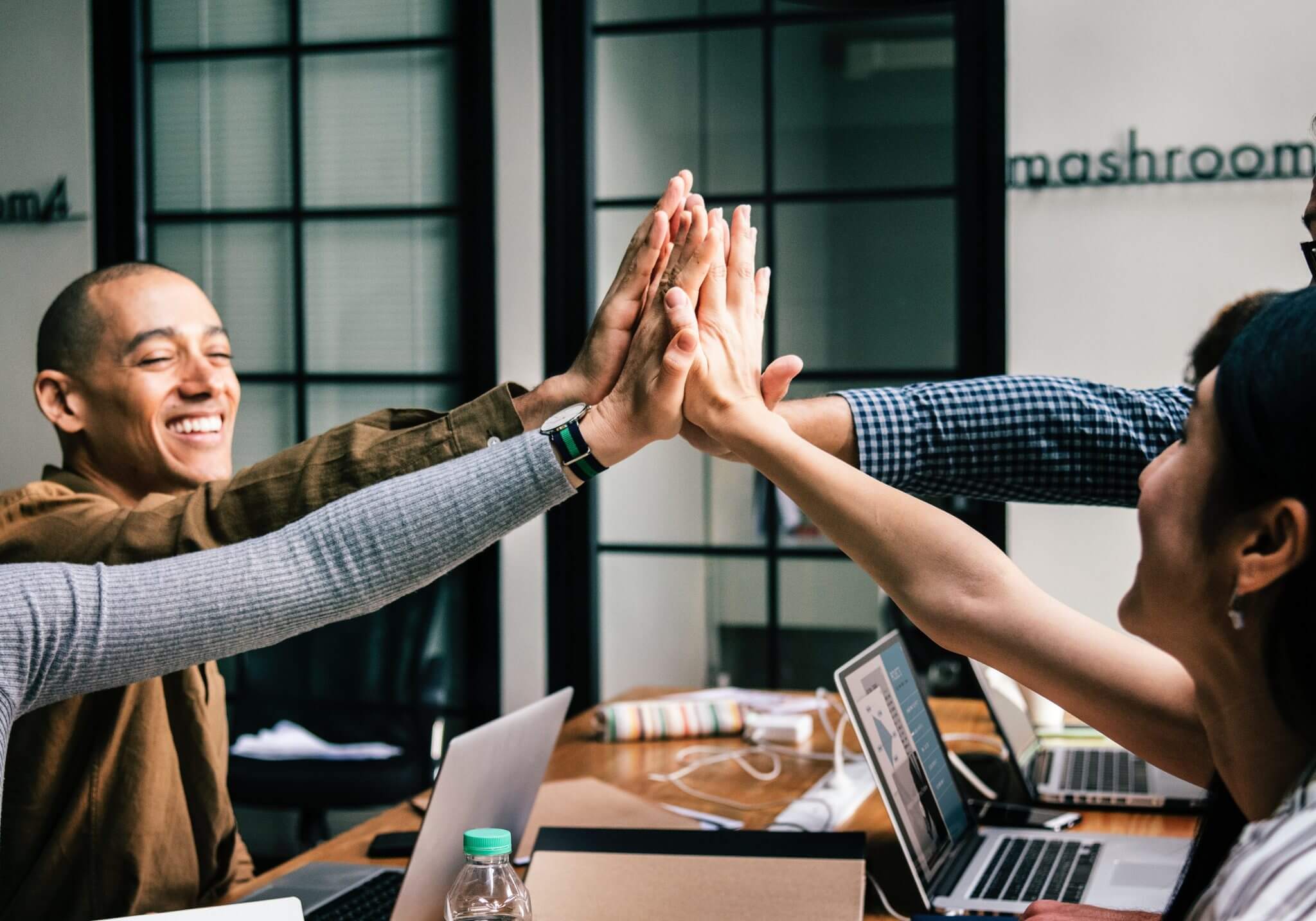 a group of employees sitting around a table high-fiving each other.
