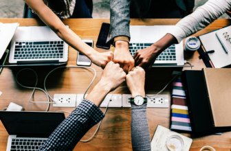 A bunch of employees sharing a fist bump over a conference table at a meeting.