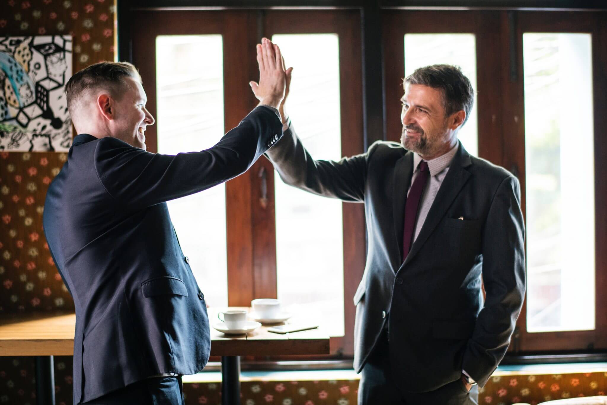 Two men in business suit attire high-fiving each other and smiling.