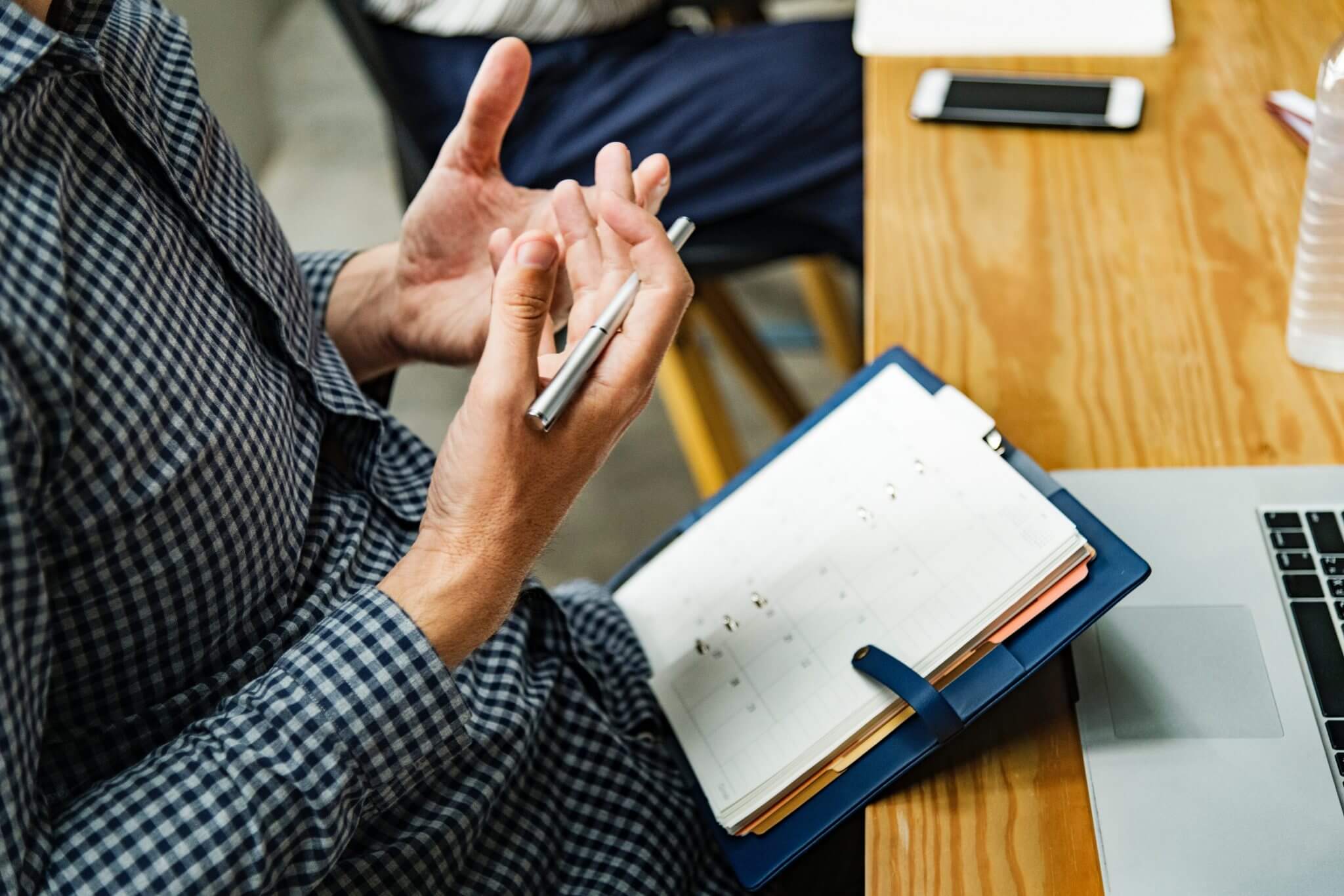 Guy sitting at a desk holding a pen and balancing a notebook in his lap, explaining something. Guy sitting at a desk holding a pen and balancing a notebook in his lap, explaining something.