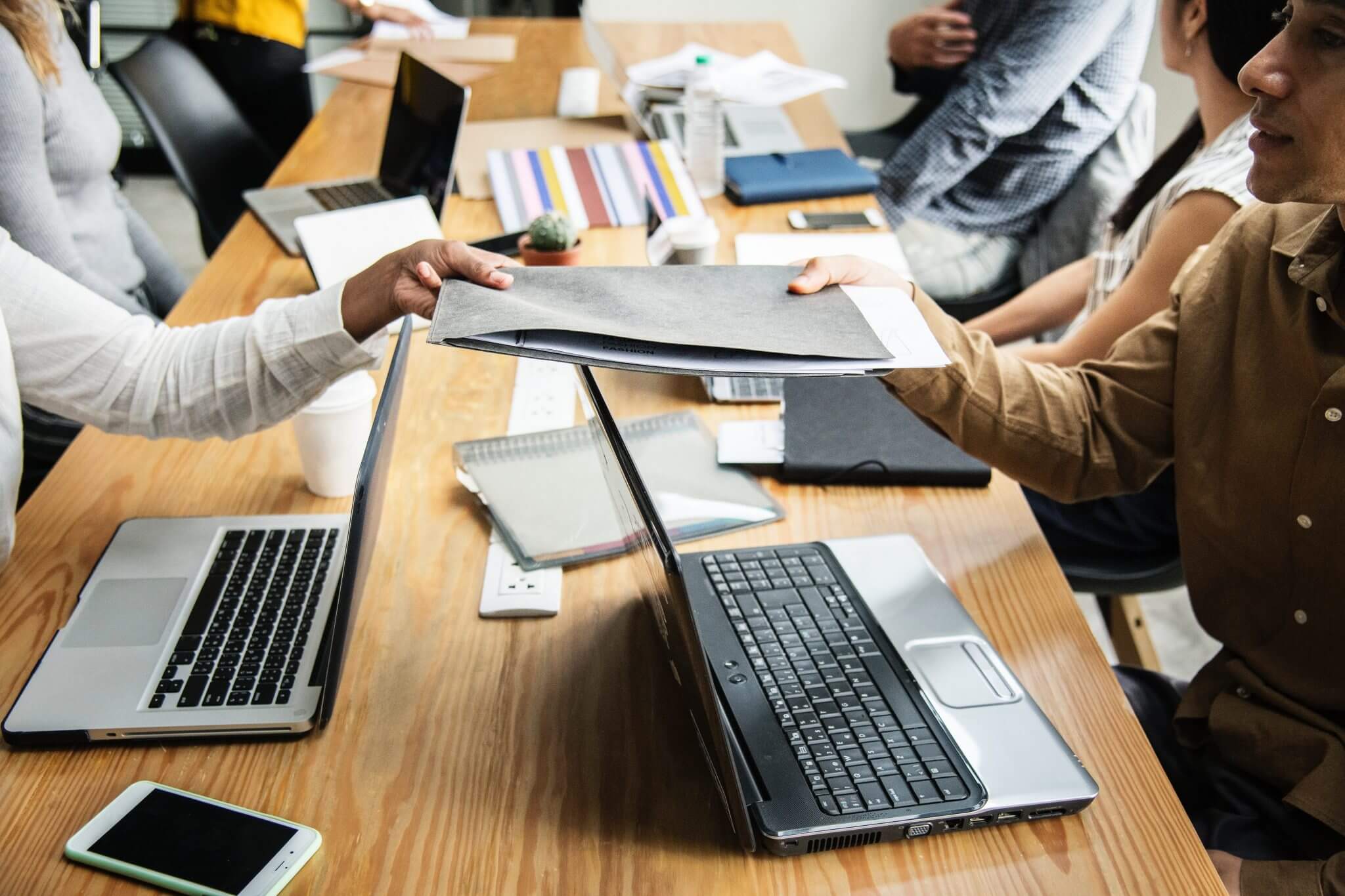 Colleagues passing a folder across a table to each other.