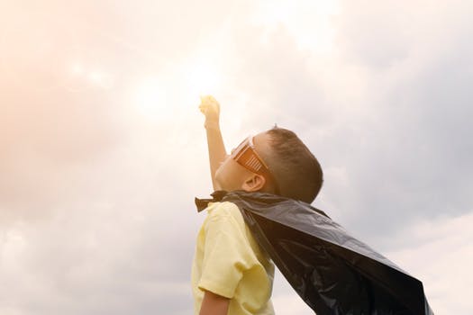 Little kid with a hero cape fist bumping the sky