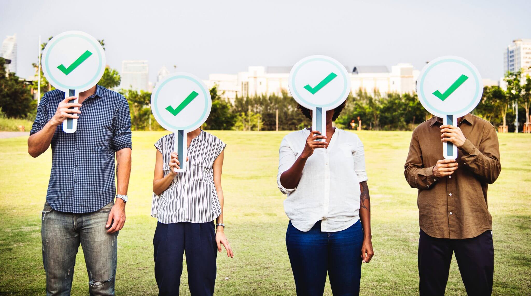 Group of 4 people standing in a field with check mark signs in front of their faces