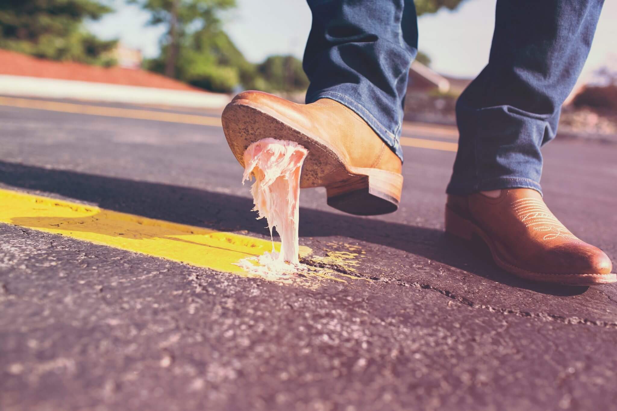 A guy in cowboy boots who just stepped on a big piece of chewing gum and the gum is stuck to the bottom of his boot.