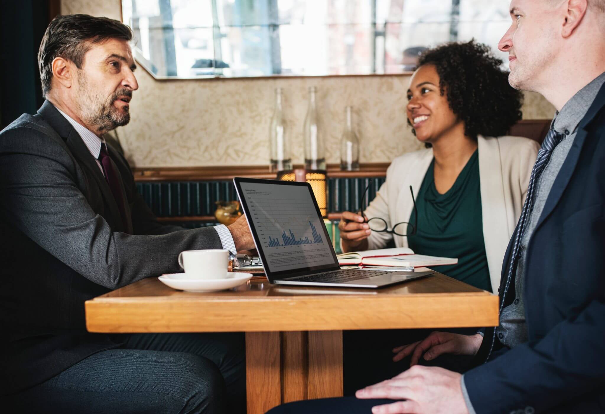 Two young employees sitting across from an older gentleman at a cafe who looks to be interviewing for a job.