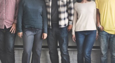 A row of people standing next to each other, camera showing only their bottom half and they are dressed in casual clothing.