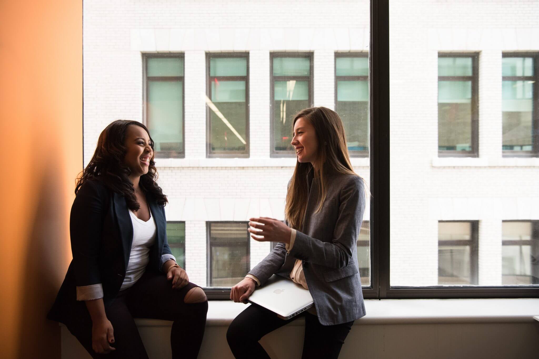 Two women sitting in front of a window talking.