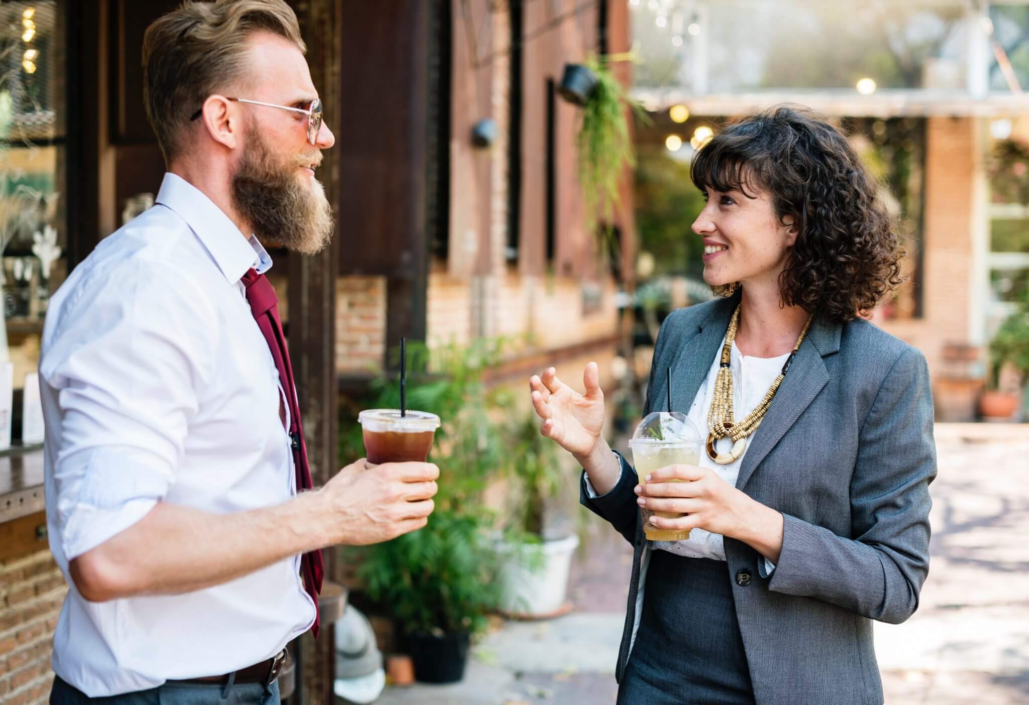 Two adults drinking coffee standing outside talking.