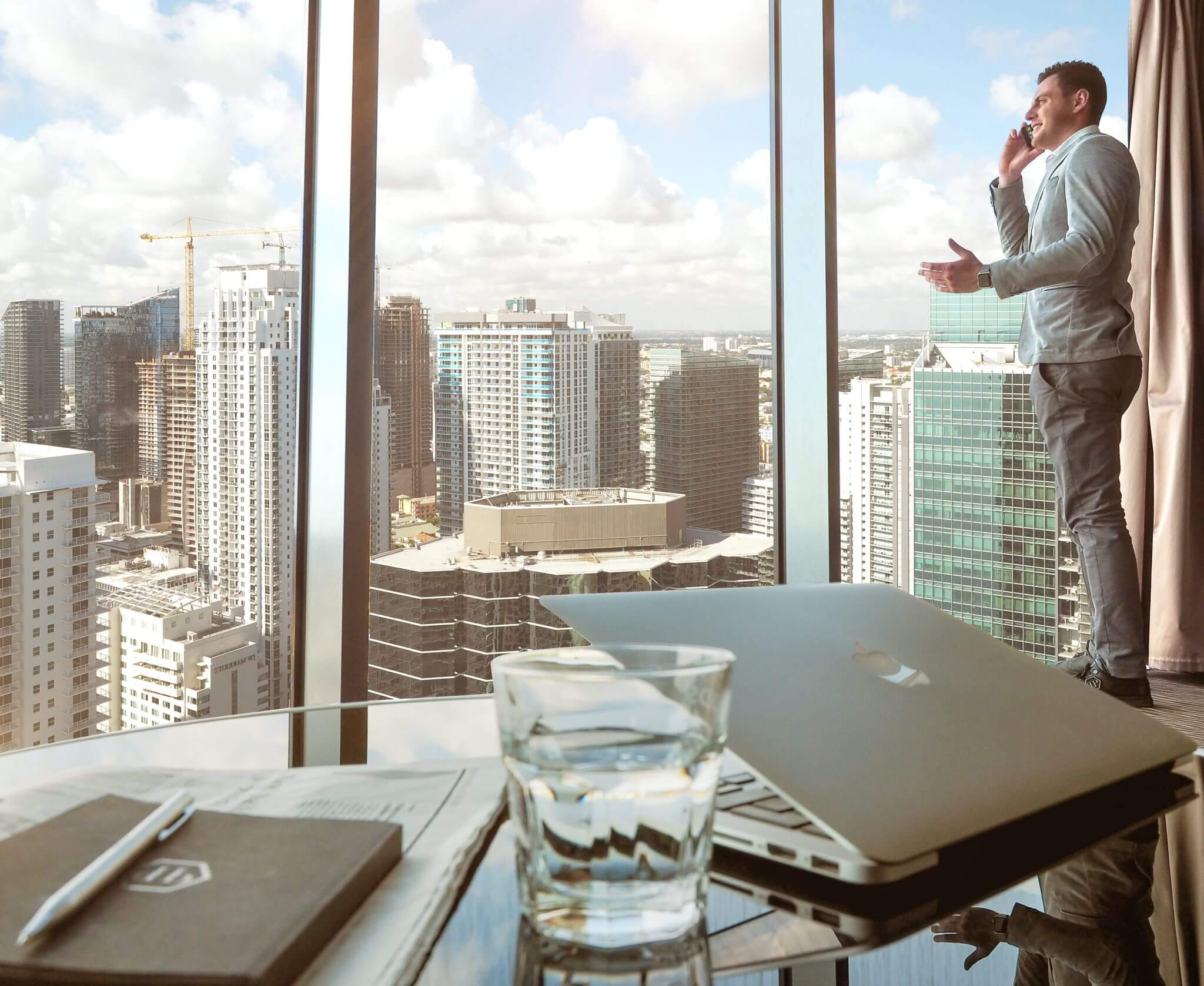 Guy standing near high-rise window talking on the phone looking out the window.