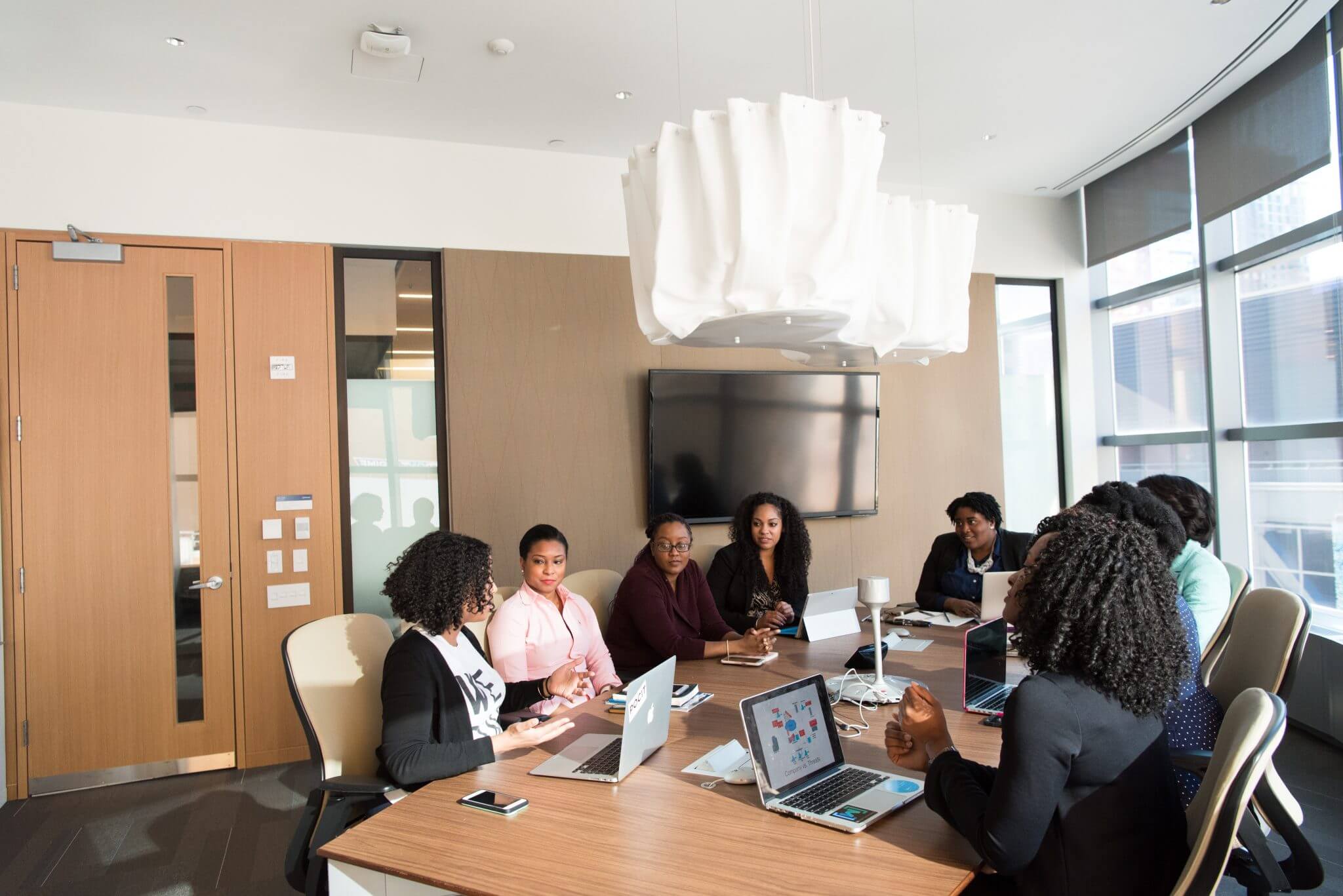 Group of employees sitting around a desk in a conference room having a discussion. Group of employees sitting around a desk in a conference room having a discussion.
