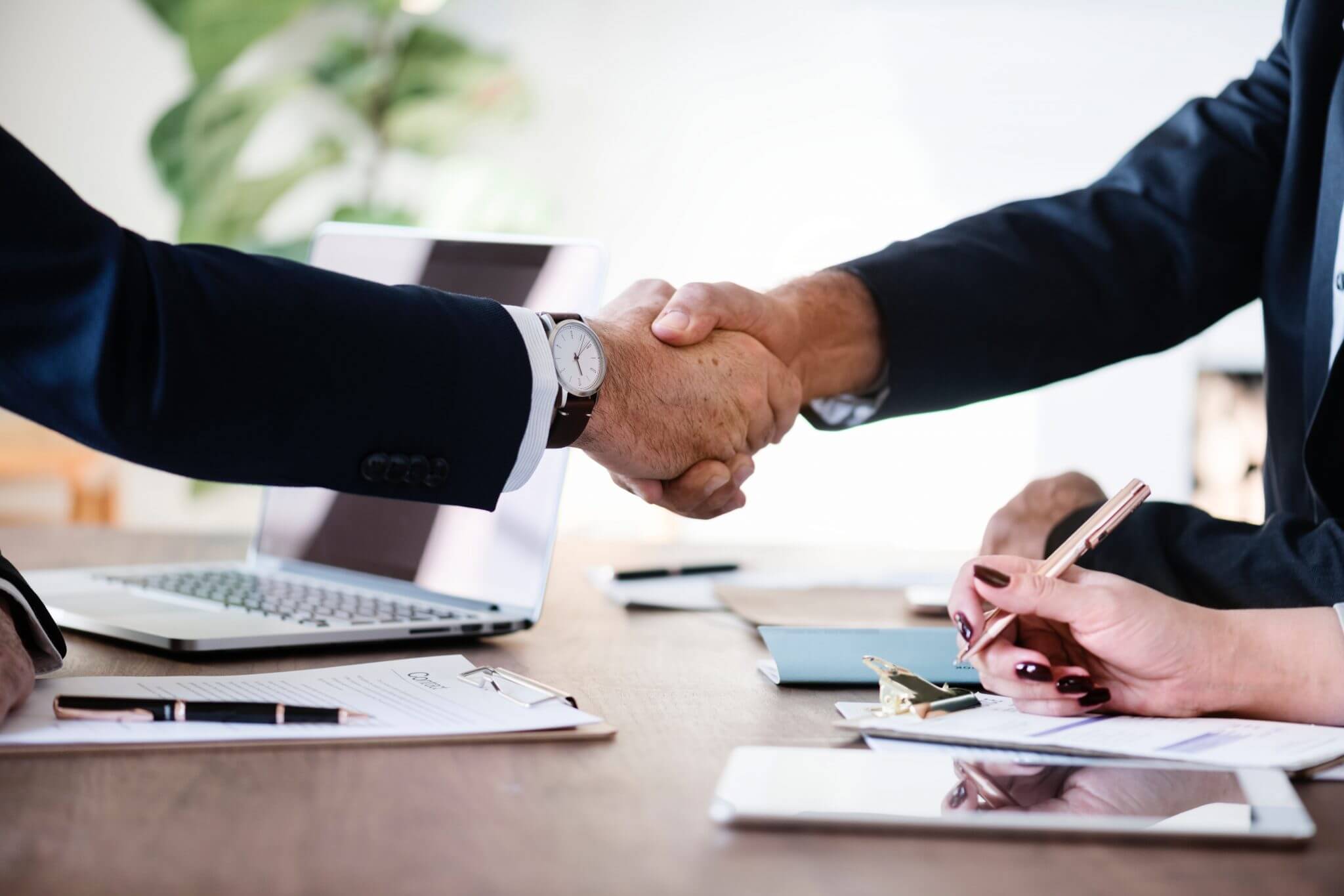 Two men in suits shaking hands over a conference table during a meeting.