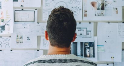 Guy staring at a board with several documents and notes attached to it. It looks like he's trying to solve a problem.