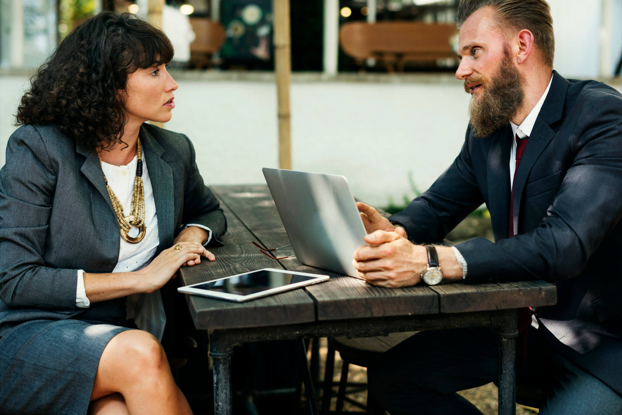Two people are sitting across a table from each other talking with a laptop.