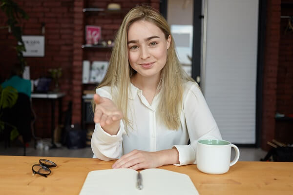Attractive young female with loose fair hair sitting at cafe tab do you have any questions interview
