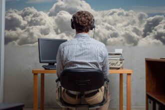 Telemarketer wearing a headset, sitting at a desk with a computer and phone, facing clouds outside the window, symbolizing focus and connection.