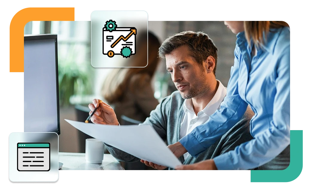 Man and woman reviewing documents in front of a desktop screen, discussing custom performance or skills reporting.