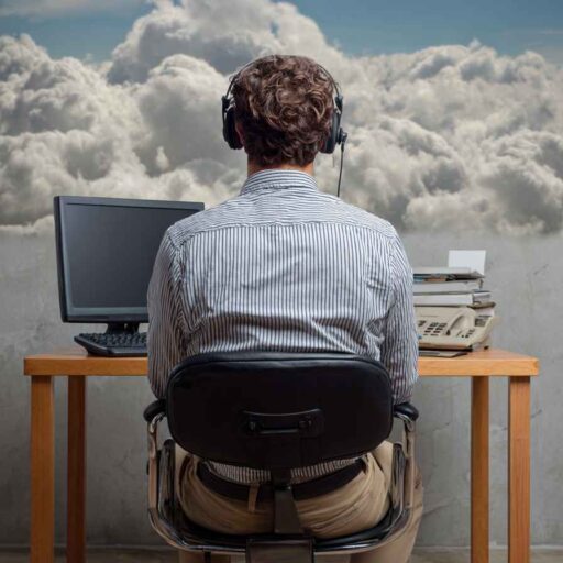 Telemarketer wearing a headset, sitting at a desk with a computer and phone, facing clouds outside the window, symbolizing focus and connection.