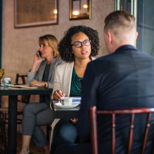 Two colleagues sitting in a restaurant. One with a displeased look on her face.