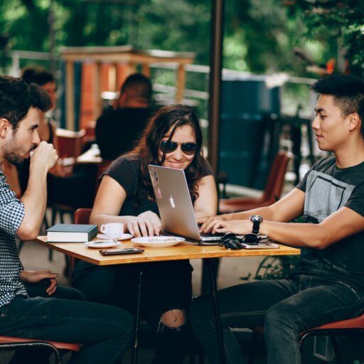 A group of friends sitting at a table laughing and talking with laptops.