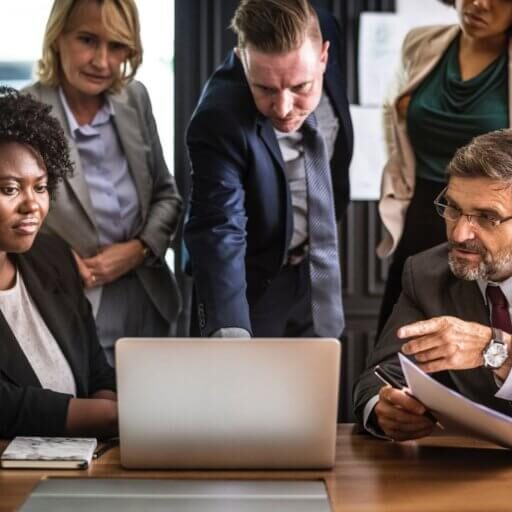 Group of people sitting around a laptop discussing something.