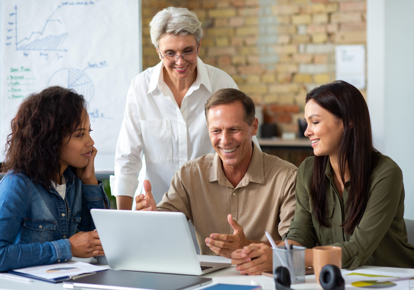 Diverse group of professionals smiling and collaborating at a laptop, ideal for aptitude assessments in leadership.