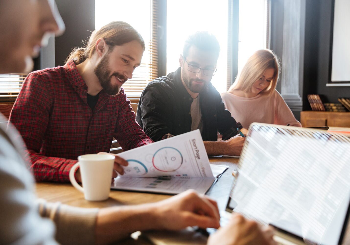 Team of young professionals reviewing assessment reports at a coworking table, illustrating the use of personality and behaviour tests in collaborative hiring.