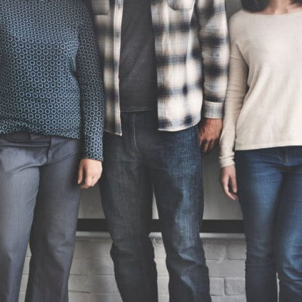 A row of people standing next to each other, camera showing only their bottom half and they are dressed in casual clothing.