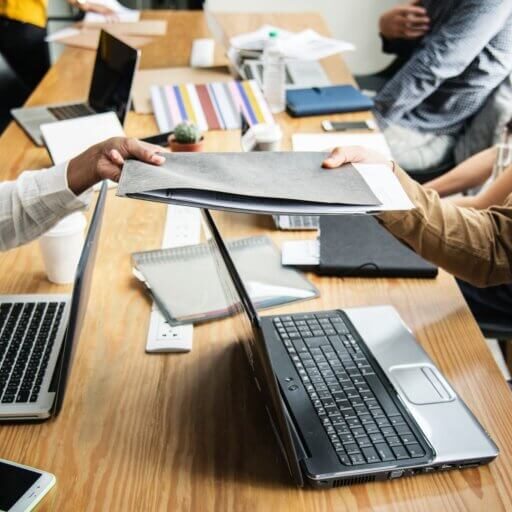 Colleagues passing a folder across a table to each other.