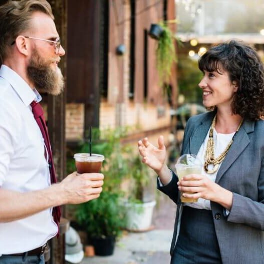 Two adults drinking coffee standing outside talking.