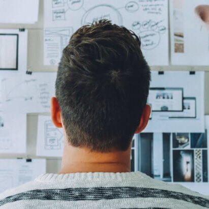 Guy staring at a board with several documents and notes attached to it. It looks like he's trying to solve a problem.
